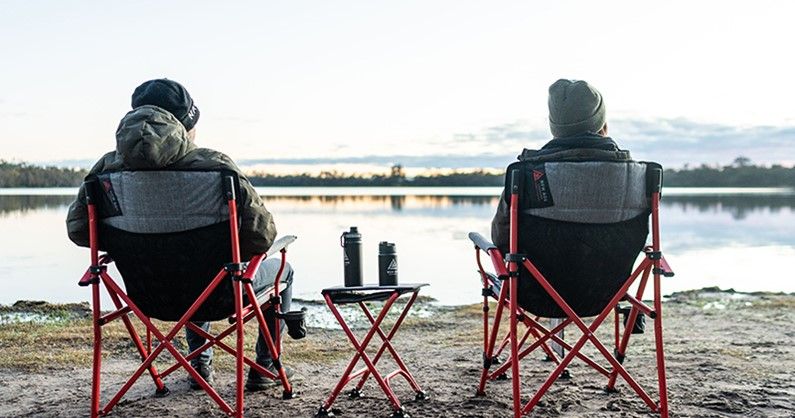Two camp chairs set up by a still lake at dawn