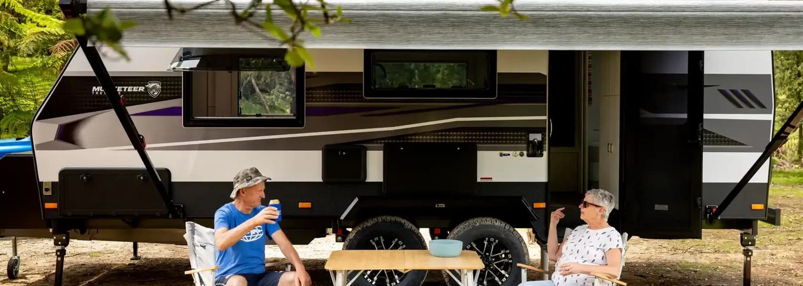 A couple relaxing under the awning of their caravan in the bush