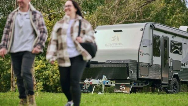 A couple walking across a campsite with their caravan behind them