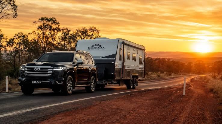 A four-wheel drive towing a caravan along an outback highway at sunset